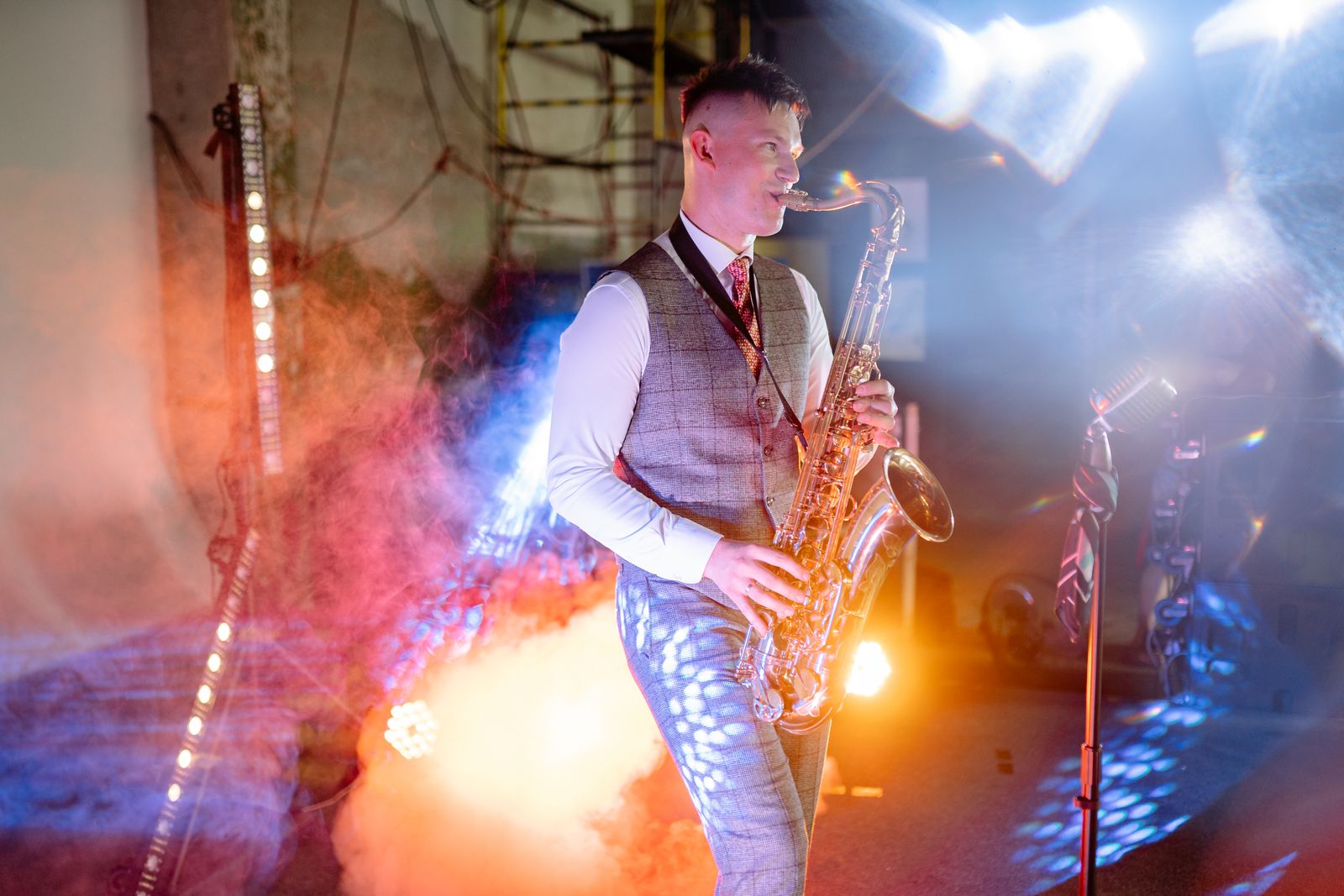 Saxofonist interpretând live pe scenă, cu fum și lumini colorate